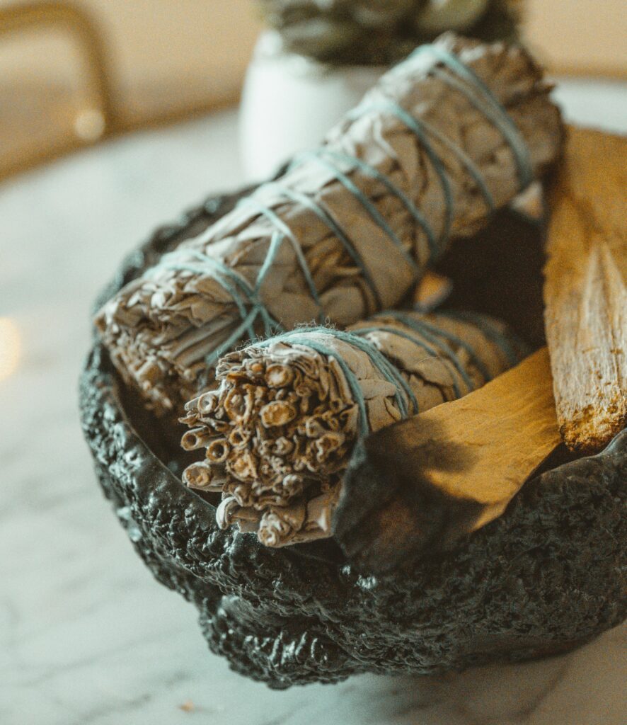 Still life of sage and palo santo in a textured bowl, perfect for smudging rituals.